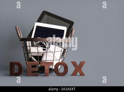 WORTENTGIFTUNG aus Holzbuchstaben und Korb mit modernen Gadgets auf grauem Hintergrund Stockfoto