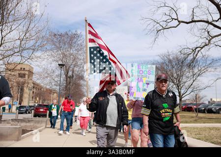 INDIANAPOLIS, INDIANA - 14. MÄRZ: Ein Vietnam-Veteran trägt eine umgedrehte amerikanische Flagge als Zeichen der Not, während US-Militärveteranen und ihre Unterstützer gegen die Kürzungen der Trump-Regierung am Department of Veterans Affairs (VA) und andere Veränderungen, die Veteranen und das Militär am 14. März 2025 betreffen, vor dem Indiana Statehouse in Indianapolis, Indiana, protestieren. Der inoffizielle Protest an der Basis wurde durch einen Flyer ausgelöst, der von der 50501-Bewegung gepostet und von Veteranen in den Vereinigten Staaten online entdeckt wurde. Quelle: Jeremy Hogan/Alamy Live News Stockfoto