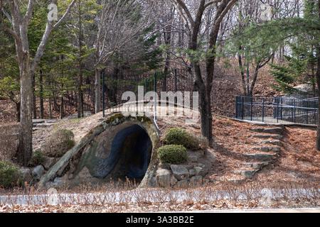 Ein Tunnelhügel, der einer Höhle ähnelt. Umgeben von Bäumen, Büschen und Steintreppen, die zu einem umzäunten Pfad führen. Im Seoul Forest Stockfoto
