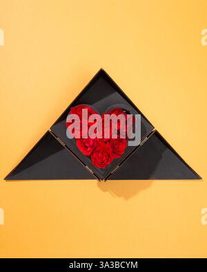 Atemberaubendes herzförmiges Arrangement aus roten Rosen in einer schwarzen dreieckigen Geschenkbox, vollständig geöffnet. Ein perfektes Symbol für Liebe und Zuneigung. Stockfoto