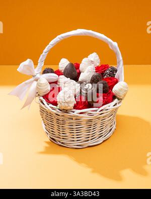 Eleganter weißer Korb gefüllt mit Erdbeeren mit Schokoladenüberzug und roten Rosen, perfekt zum Schenken Stockfoto