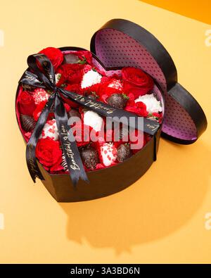 Ansicht von oben auf eine herzförmige Box mit Rosen, Schokoladenerdbeeren und Band Stockfoto