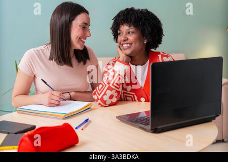 Zwei multiethnische junge Freundinnen, die zu Hause mit einem Laptop zusammen studieren Stockfoto
