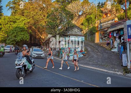 Drei junge Frauen überqueren die Straße Jalan Raya Ubud. Ubud, Bali, Indonesien. Stockfoto