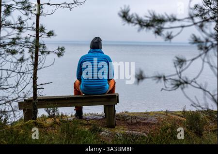 Mann, der auf einer Holzbank am See Vaettern Motala in Schweden sitzt Stockfoto