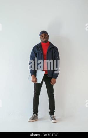 Silberfarbener Laptop in der Hand. Schwarzer Mann mit Kappe ist im Studio vor weißem Hintergrund. Stockfoto