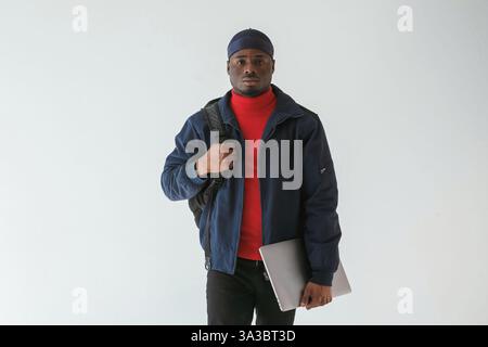 Silberfarbener Laptop in der Hand. Schwarzer Mann mit Kappe ist im Studio vor weißem Hintergrund. Stockfoto
