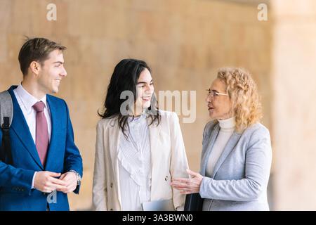 Drei Geschäftsleute führen ein freundliches Gespräch in einem Unternehmen im Freien. Sie sind in Geschäftskleidung gekleidet, lächelnd und interaktiv Stockfoto