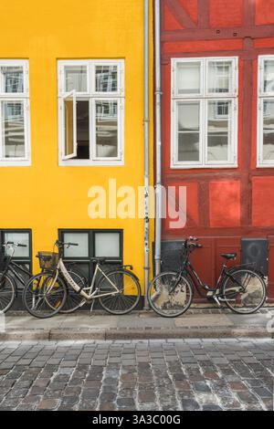 Nachhaltiger Transport, Blick auf Fahrräder, die an einer bunten Mauer in einer Kopfsteinpflasterstraße in der zentralen Altstadt von Kopenhagen, Dänemark, geparkt sind Stockfoto