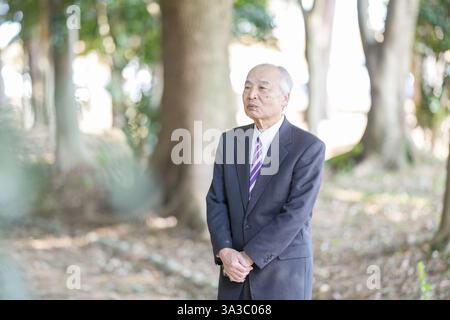 Ein Park an einem angenehmen Frühlingstag mit viel Grün in Japan. Ein Japaner in den späten 70ern, der einen Anzug trägt, steht auf. Stockfoto