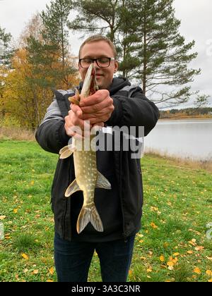 Glücklicher Mann, der frisch gefangenen Hecht mit beiden Händen hält und lächelt, Nahaufnahme Stockfoto