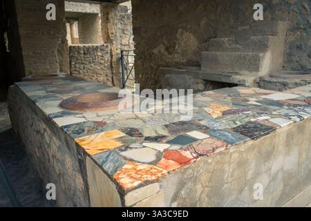 Eine historische Arbeitsplatte aus Stein mit farbenfrohen Mosaikfliesen in der antiken Stadt Pompeji, Italien, veranschaulicht Architektur und Design aus der Römerzeit. Stockfoto