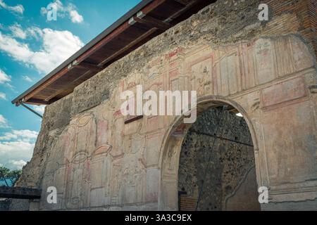 Historisches architektonisches Detail einer antiken römischen Mauer mit Fresken in Pompeji, Italien, mit bemerkenswerter Kunstfertigkeit und verwitterten Steinstrukturen. Stockfoto