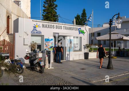 Naxos, Griechenland - 4. Oktober 2024: Naxos Bus Transfer Office in Naxos Chora, betrieben von KTEL Naxos, mit Personen und Motorrollern in der Nähe unter einem klaren bl Stockfoto