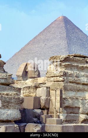 Blick auf die große Pyramide der Cheops-Pyramide von Gizeh im Hintergrund, davor Kopf der Sphinx, der über antiken Gebäudereste auf dem Gizeh-Plateau thront, Stockfoto