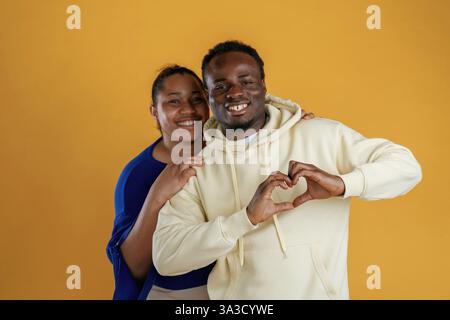 Liebesgeste zeigen. Glückliche schwarze Paare sind zusammen auf gelbem Hintergrund. Stockfoto