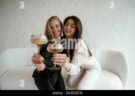 In schwarz-weißer Kleidung, mit Drink, Feiern. Zwei glückliche junge, beste Freundinnen sind drinnen. Stockfoto