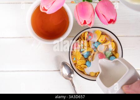 Osterfrühstück Müsli, Cornflakes mit Osterschokoladeneiern und Zuckerstreuseln, Milch oder Joghurt in Cornflakes Golden Breakfast Müsli Portion Stockfoto