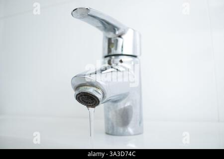 Nahaufnahme einer Armatur im Badezimmer mit fließendem Wasser und Kalkflecken und schmutzigem Waschbecken Stockfoto