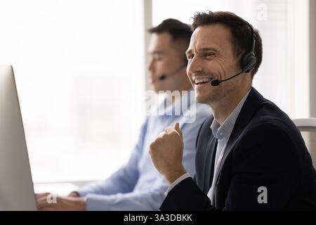 Fröhlicher Support Center-Mann mit Kopfhörern, posiert am Arbeitsplatz Stockfoto