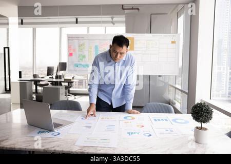 Fokussierter asiatischer Geschäftsmann, der Marketingberichte auf einem großen Bürotisch analysiert Stockfoto