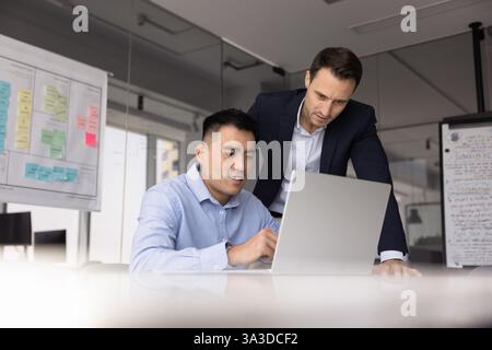 Der Vorgesetzte beobachtet den Mitarbeiter, der am Laptop arbeitet Stockfoto