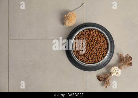 Trockenfutter-Granulat in Futterschüssel und Katzenspielzeug auf dem Boden, flach liegend. Leerzeichen für Text Stockfoto