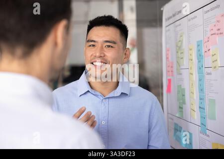 Glücklicher asiatischer Geschäftsmann, der am Whiteboard mit einem Kollegen spricht Stockfoto