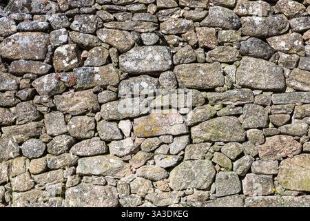 Detail einer Granitmauer mit Moos, großen und kleinen grauen Steinen, die übereinander gestapelt sind, Teil eines alten historischen Hauses Stockfoto