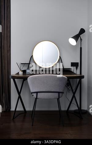Moderner Schreibtisch mit Spiegel und stilvollem grauen Stuhl in minimalistischem Zimmer Stockfoto