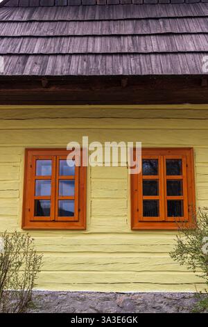 Zwei Fenster eines traditionellen gelben Holzhauses in Vlkolínec, UNESCO-Weltkulturerbe-Dorf mit horizontaler Aussicht Stockfoto