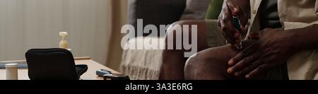 Älterer afroamerikanischer Mann, der an einem Schreibtisch sitzt und verschiedene Gegenstände darauf trägt, um einen friedlichen Moment im Zimmer festzuhalten Stockfoto