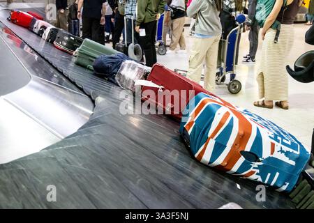 Passagiere, die am frühen Morgen auf ihr Gepäck und Gepäck warten, werden am Karussellband am Flughafen angekommen Stockfoto