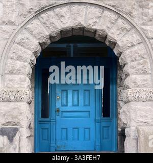 Bblue Holztür in einem historischen Steinbogen mit komplexen architektonischen Details. Stockfoto