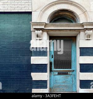 Hellblaue Holztür mit kunstvollen architektonischen Details in einer historischen Stein- und Ziegelfassade. Stockfoto