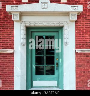Elegante grüne Glastäfelung innerhalb einer historischen roten Backsteinfassade, eingerahmt von komplizierten weißen Steinschnitzereien. Stockfoto
