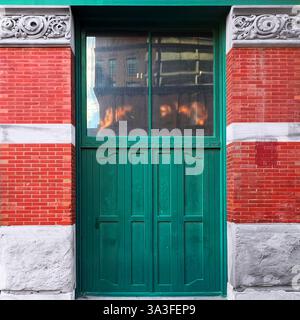 Alte grüne Tür mit großen Glaspaneelen in einer historischen roten Backsteinfassade mit filigranen Blumensteinschnitzereien. Stockfoto