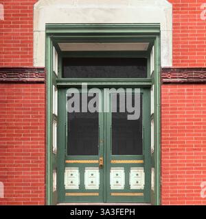 Vintage-grüne Doppeltüren mit komplizierten Paneeldetails in einer historischen roten Backsteinfassade mit dekorativen Heckfenstern. Stockfoto