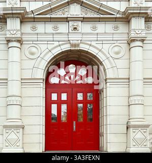 Große rote Bogentüren innerhalb einer kunstvollen neoklassizistischen Fassade mit komplizierten Steinschnitzereien und dekorativen Säulen. Stockfoto