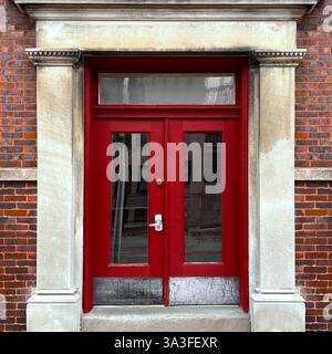 Elegante rote Doppeltüren mit Glaspaneelen in einer historischen Kalksteinfassade, die von Säulen eingerahmt ist. Stockfoto