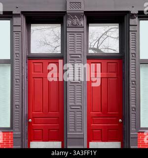 Architektonische Fassade mit roten Doppeltüren, eingerahmt von komplizierten Holzarbeiten, mit dekorativen Mustern in urbanem Ambiente. Stockfoto