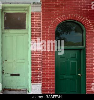Zwei kontrastierende grüne Türen aus rotem Backstein, eine veraltet und verwittert, während die andere neuere und raffinierte, die architektonische Vielfalt widerspiegeln. Stockfoto