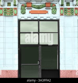 Art déco-Eingang mit Glastür innerhalb einer weiß verglasten Terrakotta-Fassade mit grünen und orangen Zierdetails, einschließlich Girlanden. Stockfoto