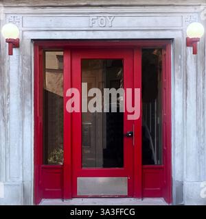 Eine auffällige rote Eingangstür in einer historischen Steinfassade mit dem eingravierten Namen „FOY“ oben, flankiert von zwei Vintage-Globus-Lichtern Stockfoto