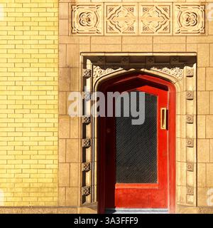 Rote Bogentür mit einer strukturierten Glasscheibe, eingerahmt von komplizierten Steinschnitzereien auf einem gelben Backsteingebäude in Chicago Stockfoto