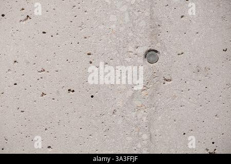 Concrete Wall Texture: Makroaufnahme einer strukturierten Betonoberfläche mit einer eingebetteten Metallscheibe, die die rauen und vielfältigen Muster zeigt Stockfoto