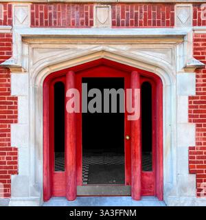 Roter Eingang im gotischen Stil, eingerahmt von komplexen Kalksteindetails, eingebettet in eine Fassade aus rotem Backstein. Stockfoto