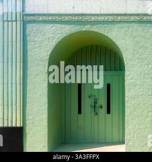 Vintage mintgrüner Bogengang mit kunstvollen Metallbeschlägen, in einer strukturierten Fassade. Stockfoto