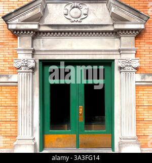 Neoklassizistischer Eingang mit grüner Doppeltür, eingerahmt von kannelierten korinthischen Säulen und einem kunstvollen Giebel, der sich in einer historischen Backsteinfassade befindet. Stockfoto