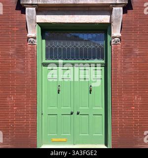 Mintgrüne Vintage-Tür mit dekorativem Buntglasfenster in einer lebhaften braunen Ziegelfassade in Chicago. Stockfoto